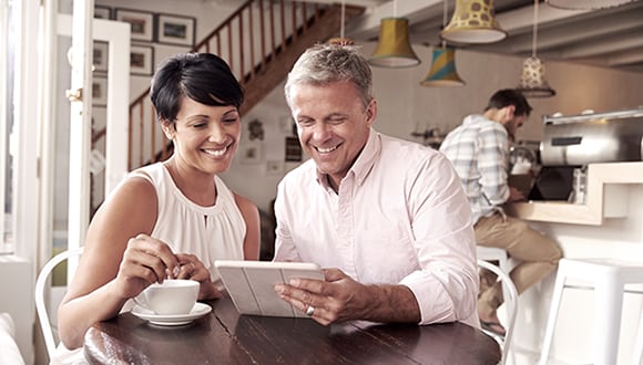 Woman and a man sitting at a table looking at the tablet screen and smiling