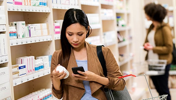 Woman in pharmacy researching medicine on phone