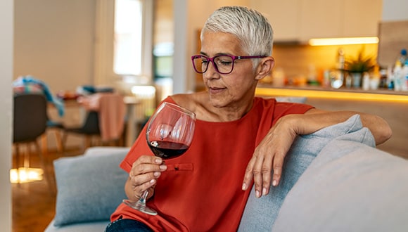 Woman sitting on the edge of her lounge drinking wine while feeling anxious at night