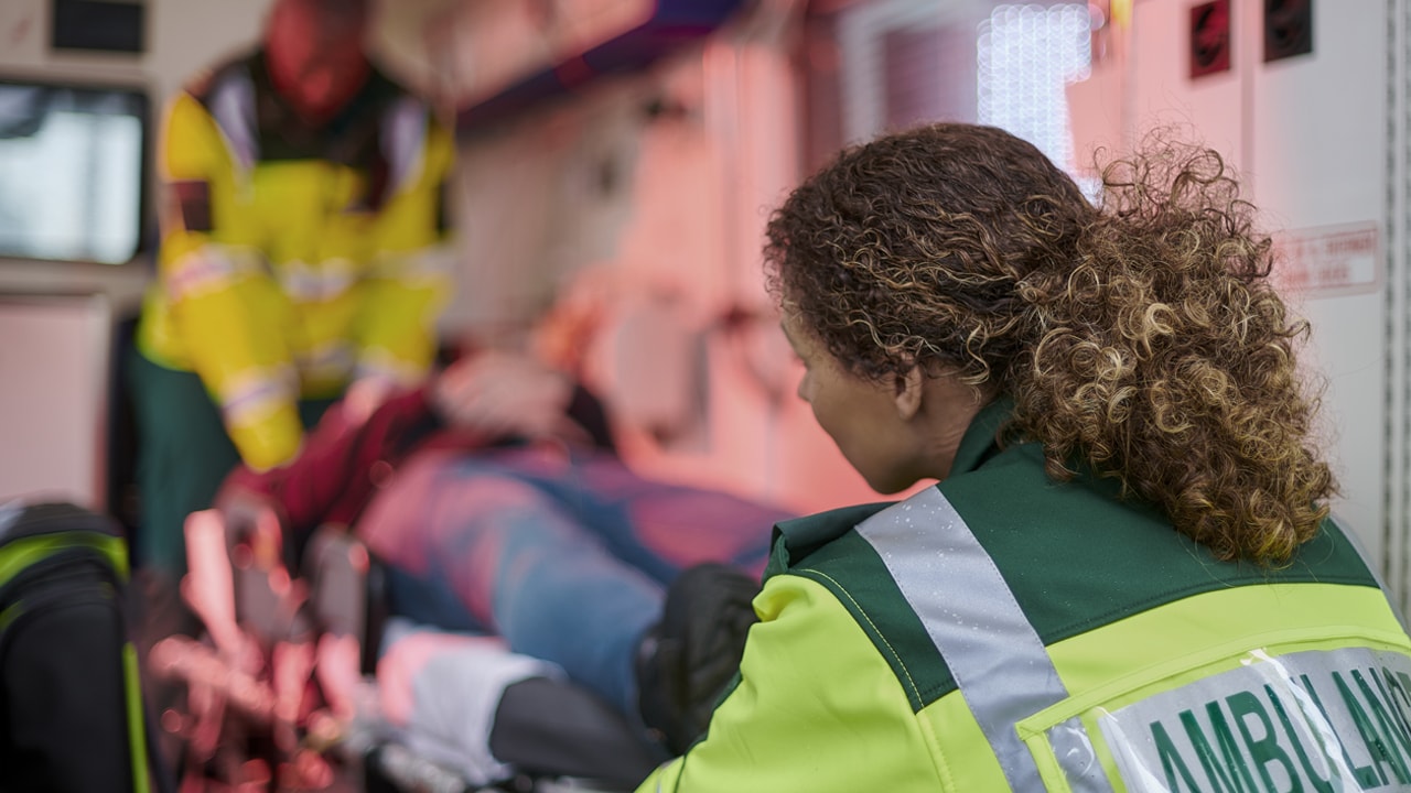  A female paramedic helps another paramedic lift a patient into an ambulance.