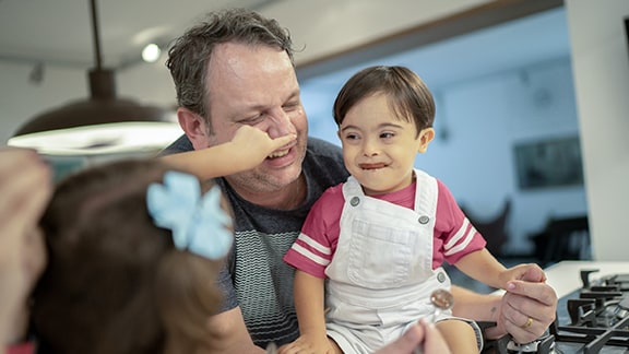 A father carries his young son who appears to have Down Syndrome