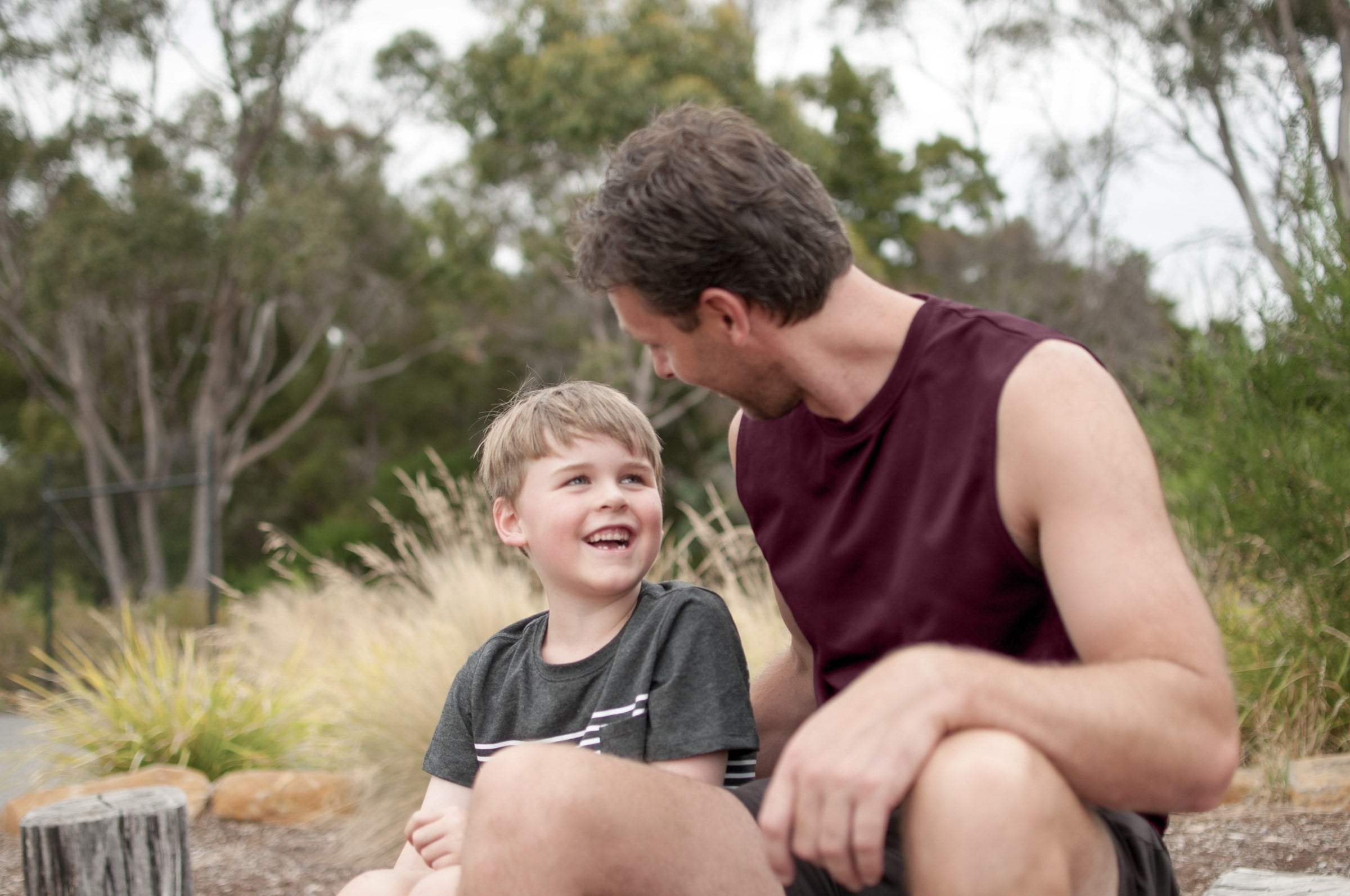 A father and son sitting next to each other outside, talking.