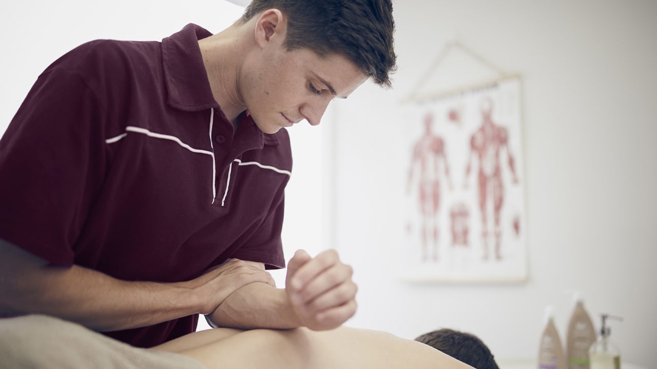 A male physiotherapist massages his clients back using his forearm.