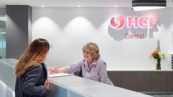 An old woman talking to a younger woman, with a HCF insurance logo on the wall behind them.